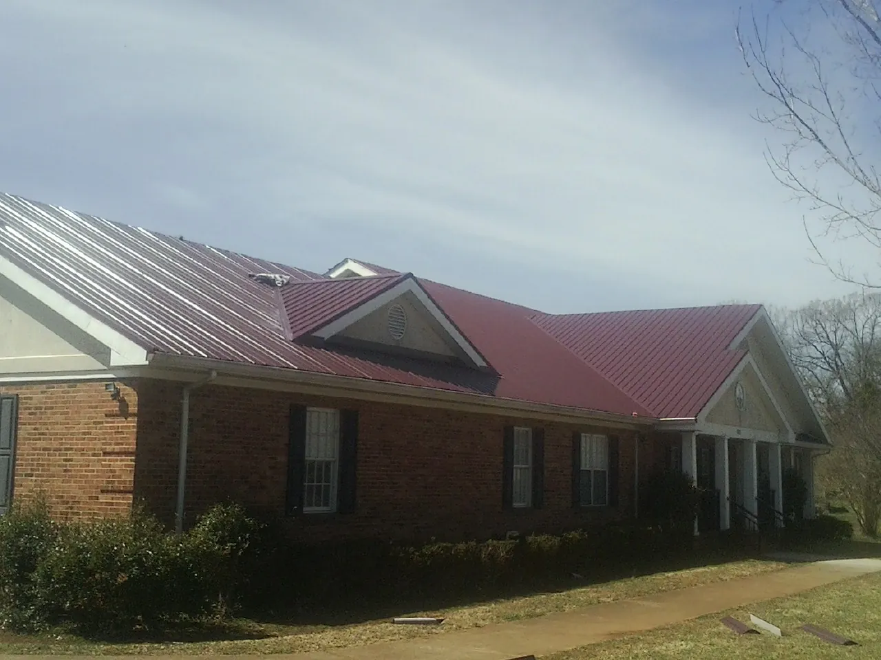 Red metal roof with gabled entries on a long brick building, from a Hail Damage Roof Repair job in Cedar Key