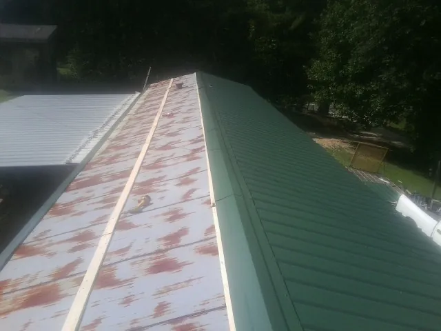 Old rusted panels beside newly installed green metal roofing — Wind Damage Roof Repair by Roofing Brothers in Cedar Key